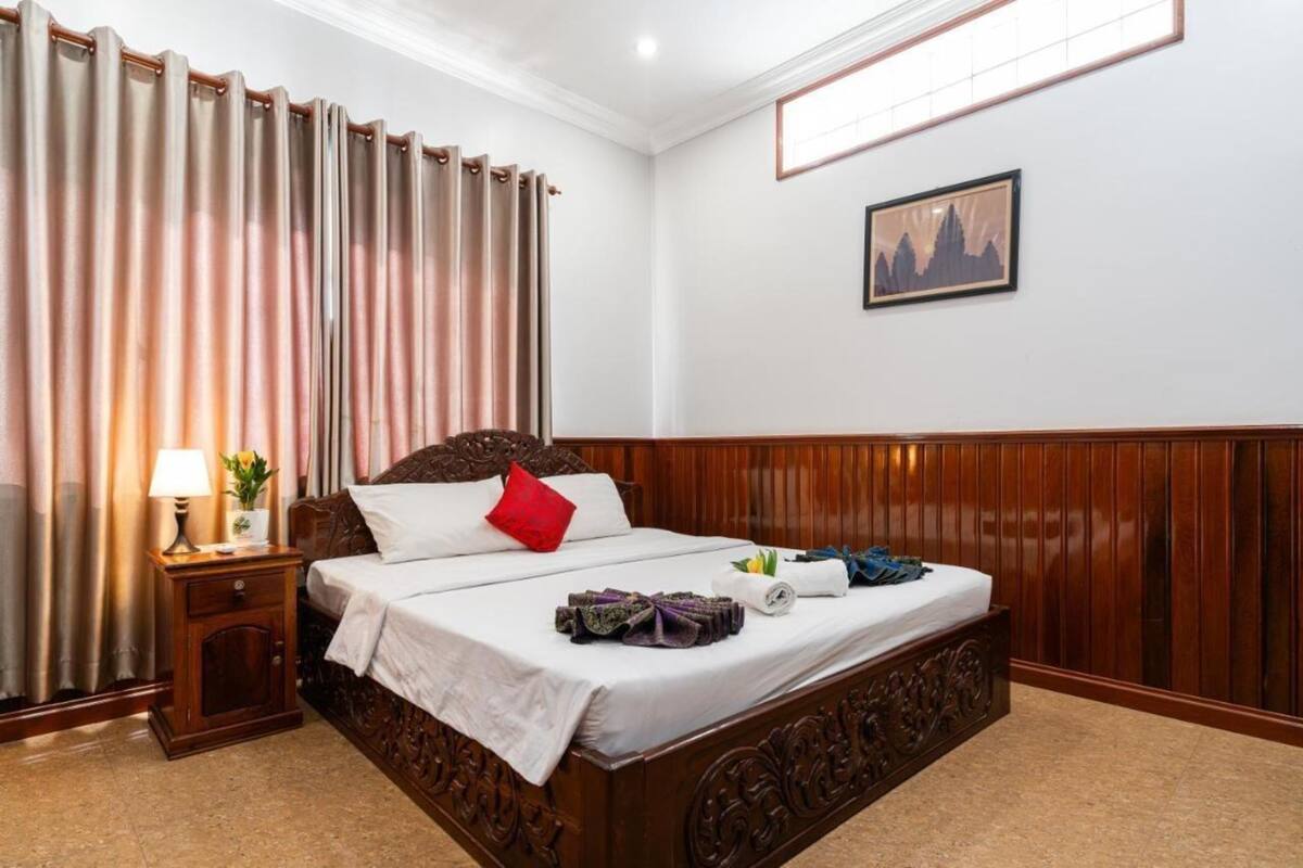 Quarto de hotel com uma cama de madeira, uma mesa de cabeceira com abajur e um quadro na parede.