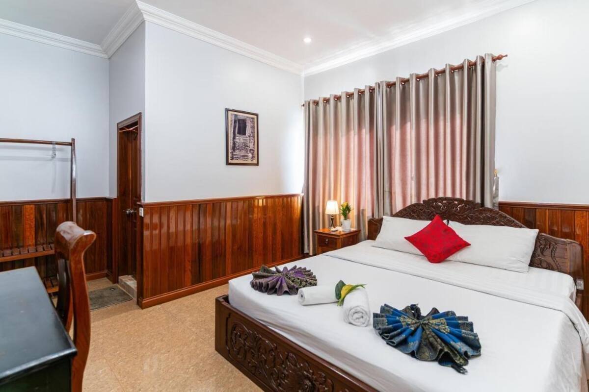 Quarto de hotel com cama de madeira, mesa de cabeceira com luminária, cadeira de madeira e guarda-roupa.
