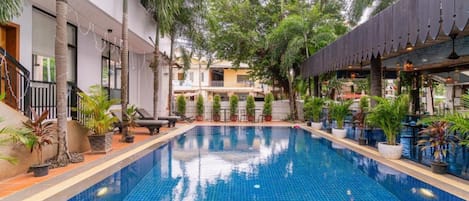 A swimming pool with tiled blue water, surrounded by potted plants and palm trees.