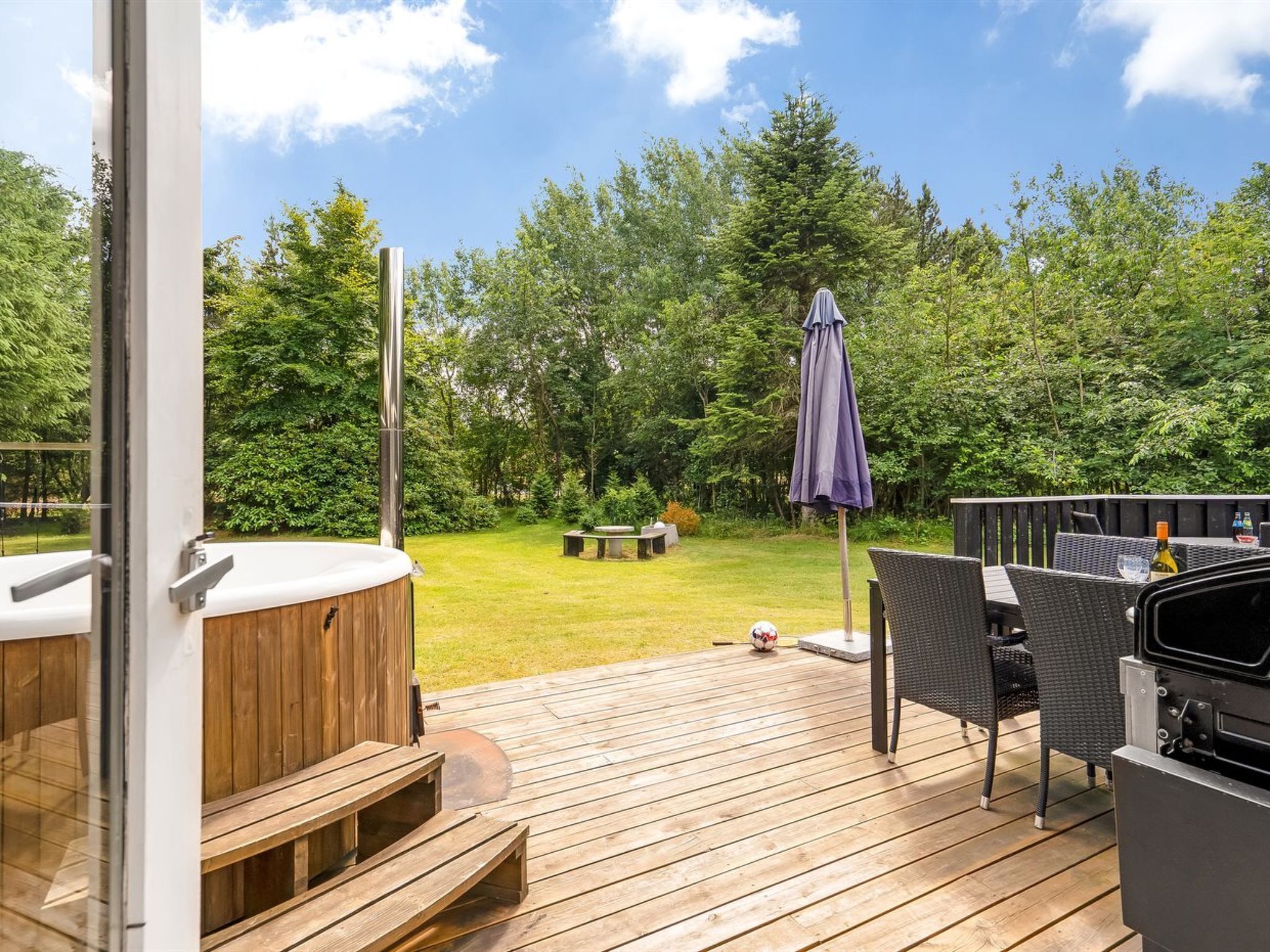 Una terraza al aire libre con jacuzzi, mobiliario exterior y vista a zona boscosa.