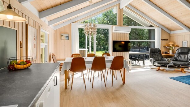 Un vaste espace de salle à manger avec un haut plafond et de grandes fenêtres, une cuisine équipée d’appareils électroménagers modernes et un coin salon confortable avec des fauteuils en cuir.