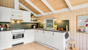Une cuisine moderne avec des meubles blancs, un plafond en bois et un petit tabouret.