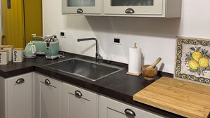 Une cuisine avec des meubles blancs, un plan de travail noir, un mur d’accent en pierre, un réfrigérateur jaune et une planche à découper en bois.