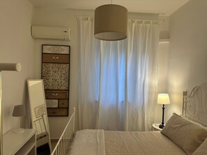 A bedroom with a bed, a bedside table with a lamp, a wall-mounted air conditioner, and a curtain. - Cozy apartment also suitable for families located in the heart of Palermo  (Palermo)