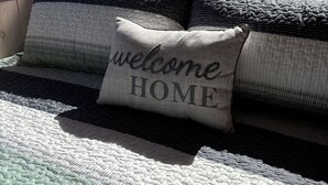 A bed with a quilt and pillows, including one with "welcome HOME" text, in a room with a window and a view of trees and a dog. - Ranch style living with incredible views! (Cambria)