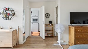 Une cuisine moderne avec des armoires blanches, un four encastré et un four à micro-ondes. On y trouve un coin repas avec une table et des chaises en bois. Un grand téléviseur à écran plat est fixé au mur.