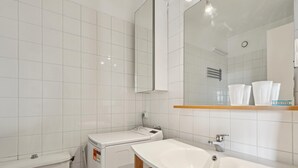 Une salle de bain moderne avec un lavabo blanc, un miroir et des toilettes. On y trouve également une machine à laver et un porte-serviettes fixés au mur.