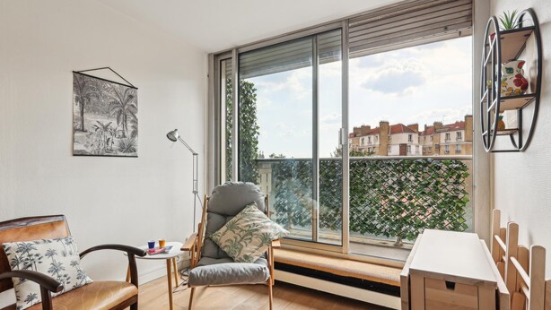 Un salon moderne avec une grande fenêtre, un canapé, un fauteuil, une petite table et un radiateur.