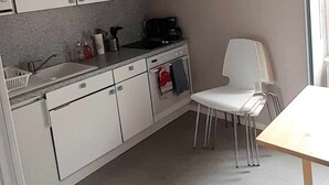 Keittiössä on valkoiset kaapit, valkoinen tuoli ja puinen pöytä.