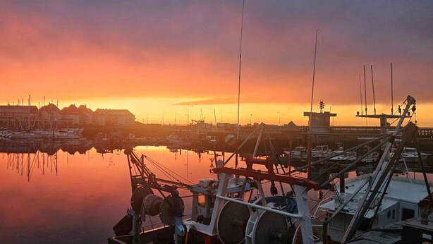 Satamassa on laivoja, ohjaustorni ja taustalla näkyy rakennuksia auringonlaskun aikaan.