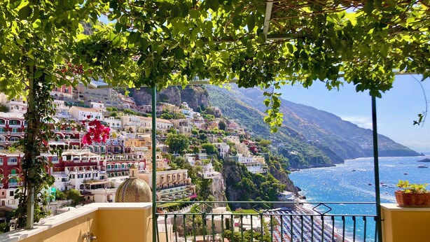 Un balcon donnant sur une ville côtière, avec des bâtiments à étages et une plage parsemée de parasols.