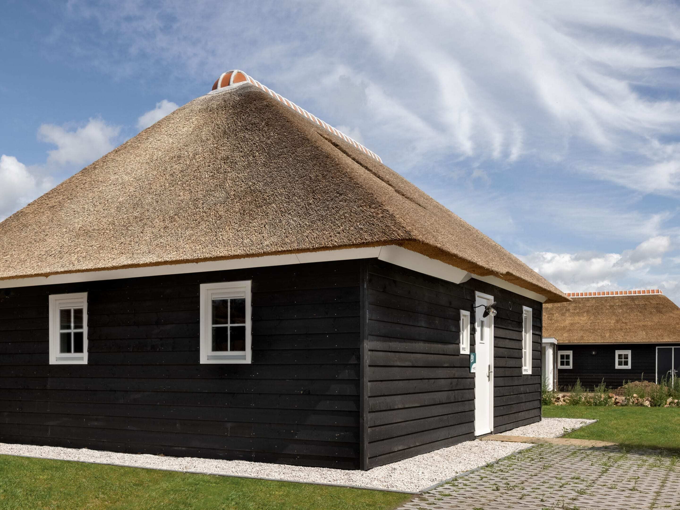 A black wooden building with a thatched roof and white trim, featuring a small window and a door.