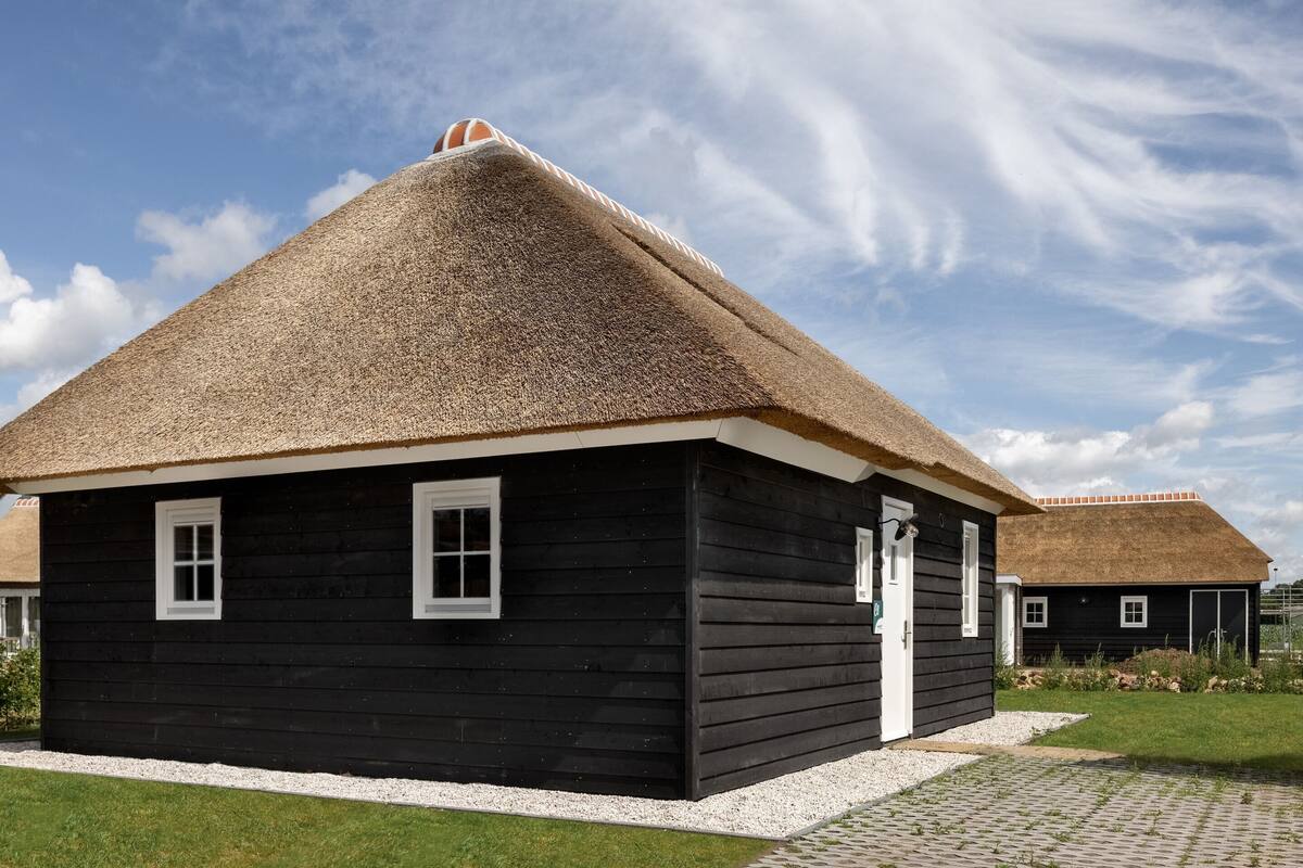 A black wooden building with a thatched roof, white windows, and a gravel pathway.