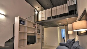 A modern hotel room with a sofa, a TV on a stand, a staircase, and a bookshelf. - Lovely apartment for 4 people with A/C, WIFI, TV and patio (Milan)