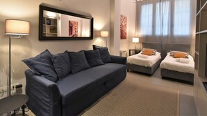 A modern hotel room with a dark blue sofa, two single beds, a large mirror, and a view of a building through the window. - Lovely apartment for 4 people with A/C, WIFI, TV and patio (Milan)