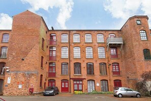 A multi-story brick building with red doors and windows, a car parked in front, and a clear sky. - Raleigh Square-2BR Ground-Floor Apt in Nottingham (Nottingham)