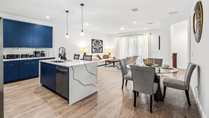 A modern kitchen with blue cabinets, a marble island, and a dining area with a glass table and grey chairs.