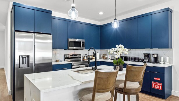 A modern kitchen with blue cabinets, stainless steel appliances, and a central island with two bar stools.