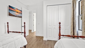 A bedroom with two wooden beds, a white door, and a painting of a sunset on the wall.