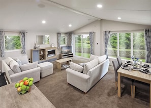 A modern living room with a sofa set, a TV, a dining table set for four, and a large window with curtains.
