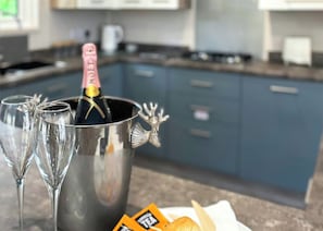 A kitchen with a metallic container holding a bottle and glasses, and a packet of tea on the counter.
