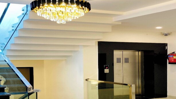 Un interno moderno con una scala, un lampadario, un ascensore e un estintore.