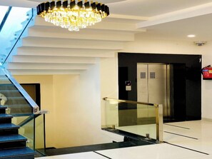 Ein modernes Interieur mit Treppe, einer Kandelaberleuchte, einem Aufzug und einem Feuerlöscher.
