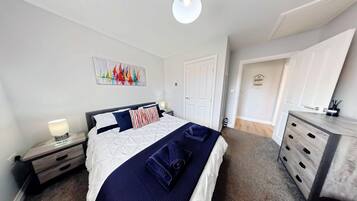Un dormitorio con cama, mesita de noche, cómoda, un cuadro en la pared y una puerta que da a otra habitación.
