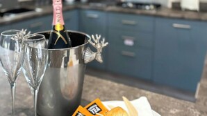 Eine Küche mit einem metallenen Behälter, der eine Flasche und Gläser enthält, und einem Teller mit Teebeuteln und einem Servietttuch.