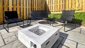 Eine Terrassengruppe im Freien mit einem quadratischen Tisch, zwei schwarzen Stühlen und einem Holzzaun im Hintergrund.
