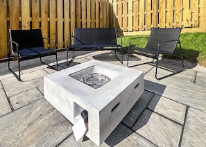 Eine Terrassengruppe im Freien mit einem quadratischen Tisch, zwei schwarzen Stühlen und einem Holzzaun im Hintergrund.