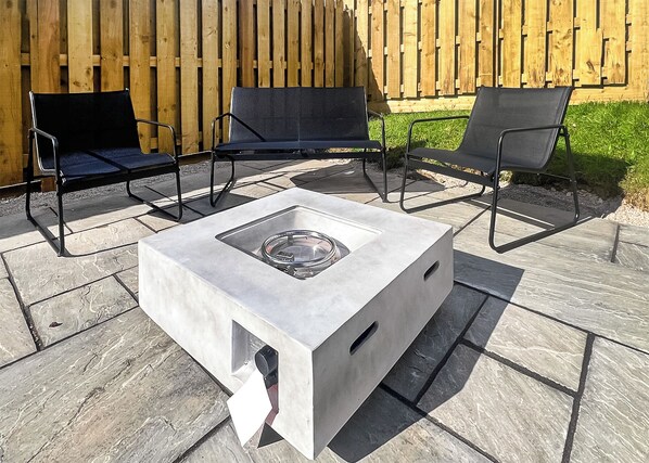 An outdoor patio with a square table, two black chairs, and a wooden fence in the background.