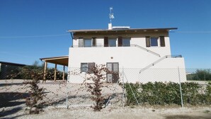 A two-story building with a flat roof, a covered porch, and a fenced yard. - Farmhouse in Marche with Pool and Coastal Views (Fermo)