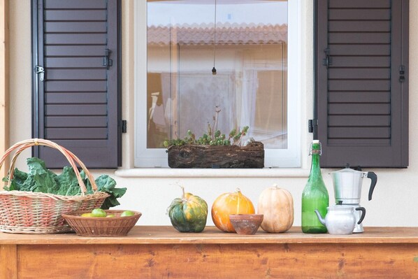 A window with shutters, a wooden shelf with various items including a basket, a green bottle, and a metal pot.