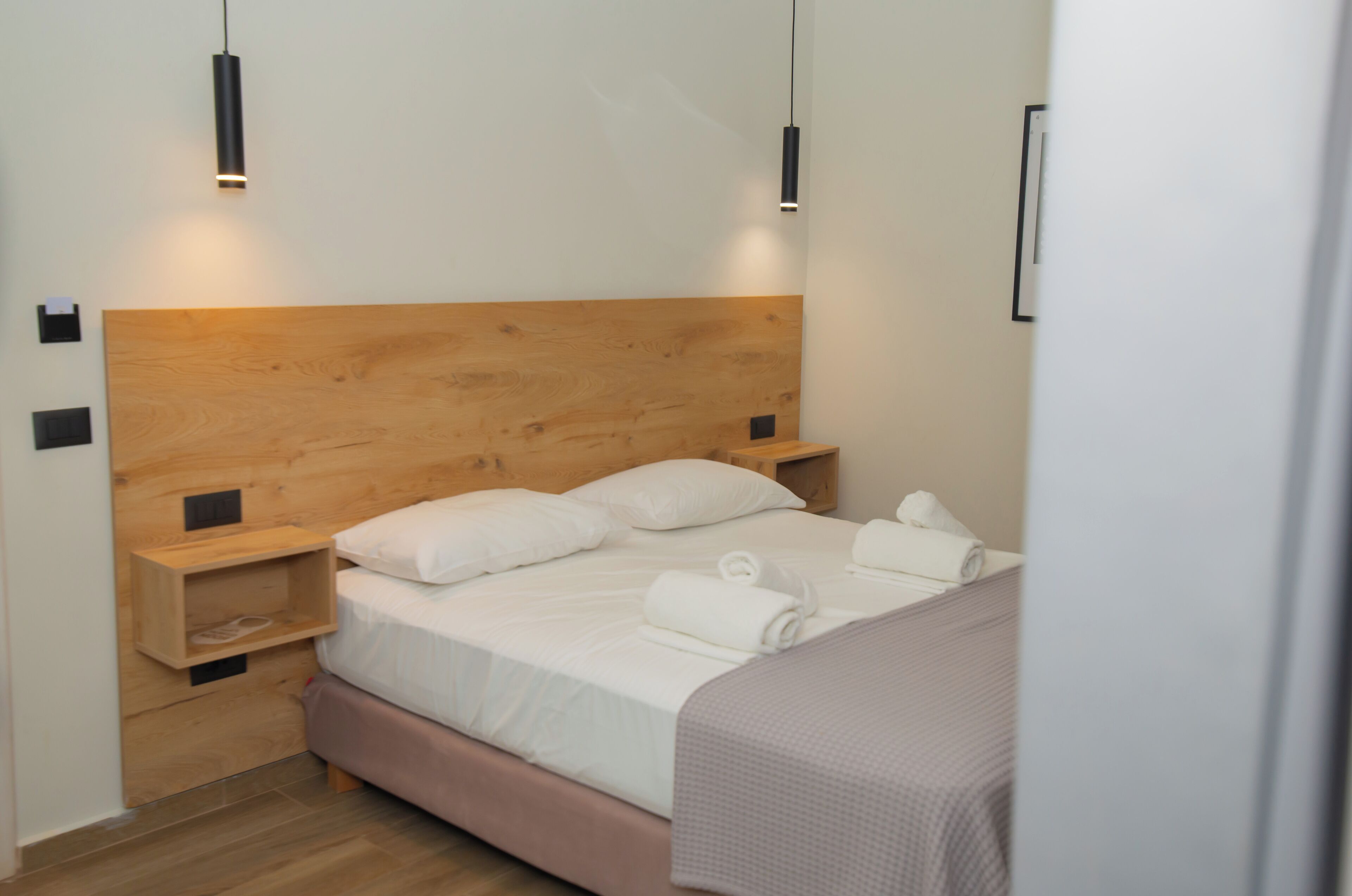 Una cama bien hecha con sábanas y almohadas blancas, un cabecero de madera y dos mesitas de noche con lámparas negras.