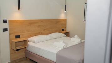 Una cama bien hecha con sábanas y almohadas blancas, un cabecero de madera y dos mesitas de noche con lámparas negras.