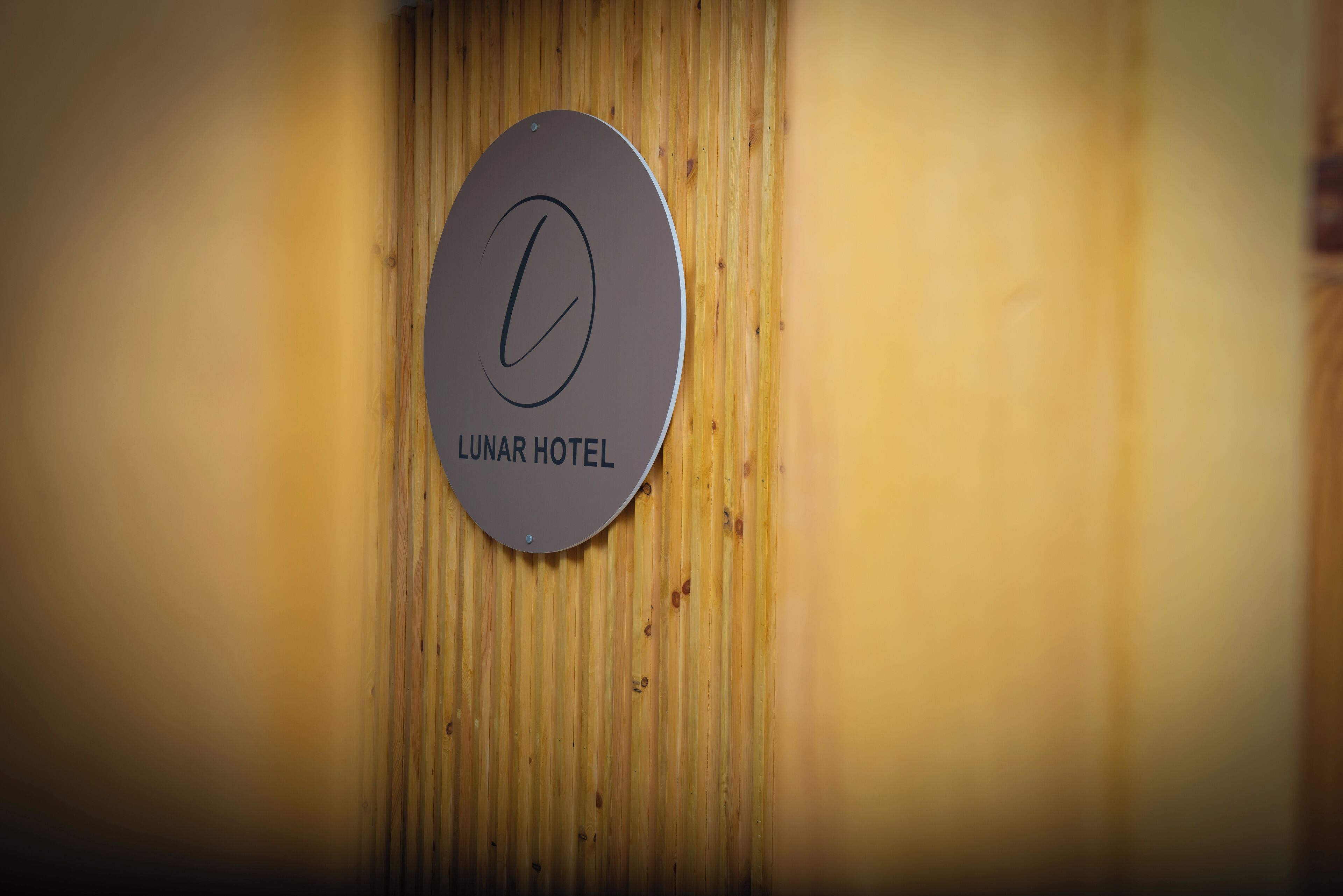 Segno circolare con una 'L' stilizzata e il testo 'LUNAR HOTEL' su un muro di legno.