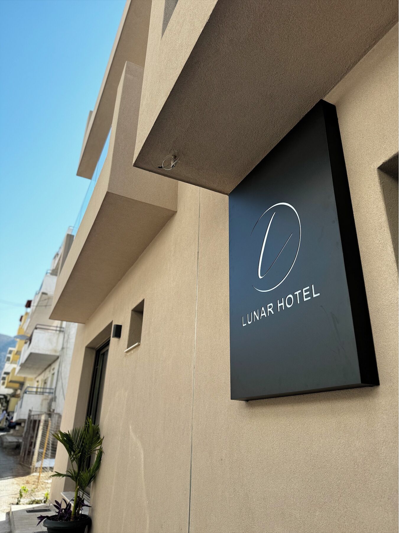 A modern hotel sign with a minimalist design, featuring a circular logo and the name "Lunar Hotel" on a dark background.