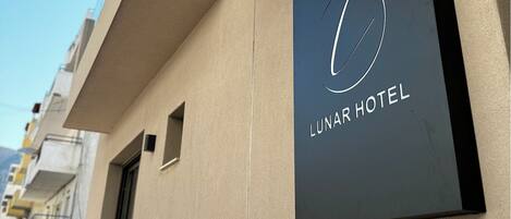 A modern hotel sign with a minimalist design, featuring a circular logo and the name "Lunar Hotel" on a dark background.
