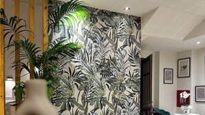 Un soggiorno moderno con una parete decorata con un motivo a foglia tropicale, un divano con cuscini, un tavolino da caffè e un'area pranzo con sedie.