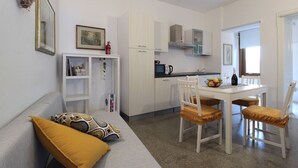 A compact living space with a kitchenette, a dining area with a table and chairs, a sofa with cushions, and a bookshelf. - Lovely apartment for 2 people with sauna, WIFI, A/C, TV and balcony (Valdobbiadene)