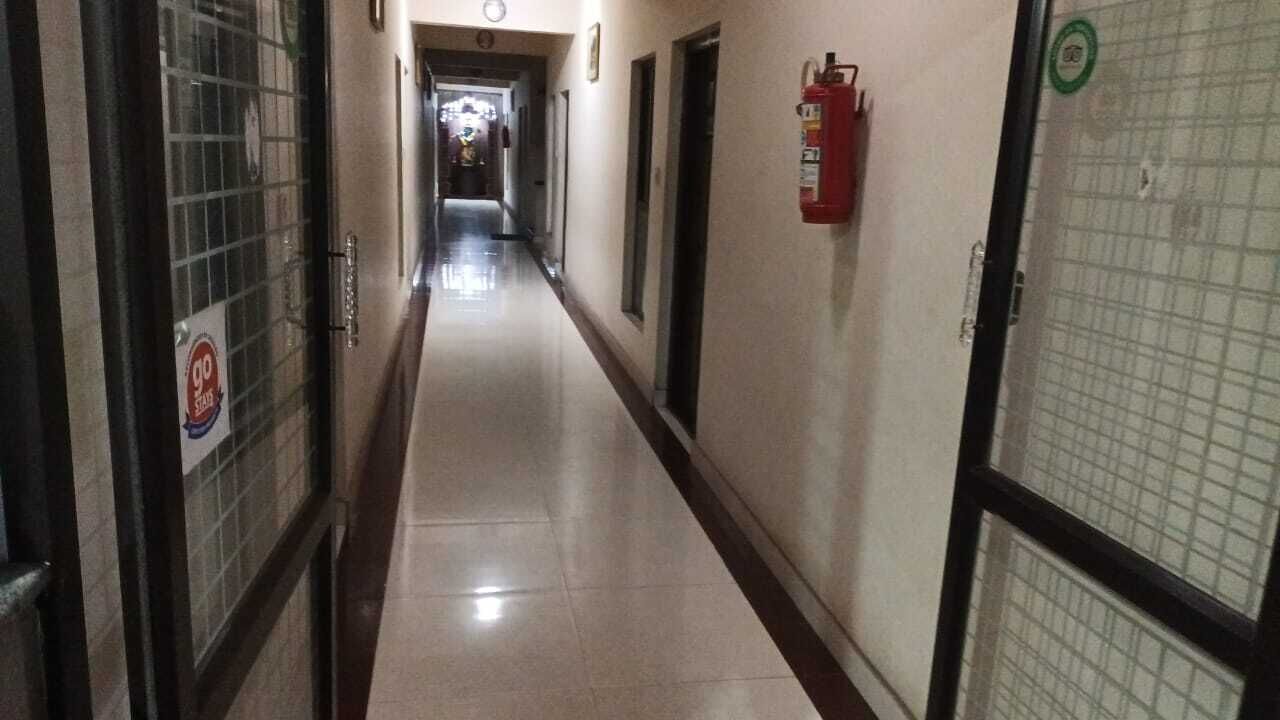 A long, narrow hallway with doors on both sides, a fire extinguisher mounted on the wall, and a sign on the left door.
