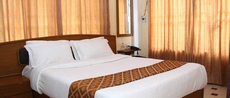 Una habitación de hotel con una cama grande, un cabecero de madera, una mesita de noche, un espejo y cortinas.