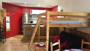 Une pièce compacte comprenant un lit superposé, un coin cuisine et un espace repas.