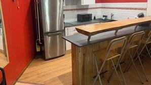 Une cuisine compacte équipée d’un réfrigérateur en acier inoxydable, d’un four à micro-ondes et d’un comptoir-bar en bois avec des tabourets.