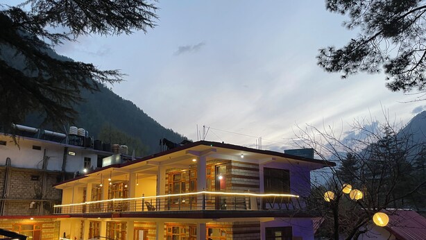 A two-story building with a balcony, outdoor seating, and a view of the mountains. - Woodward Magique kasol (Bhuntar)