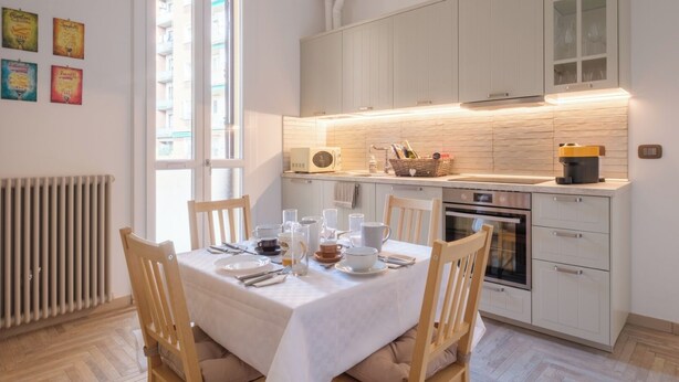 Una cocina moderna con armarios blancos, una mesa de comedor para cuatro personas y un ventanal que proporciona luz natural.