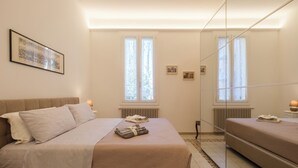 Un dormitorio con cama, mesitas de noche, un espejo y dos ventanas.