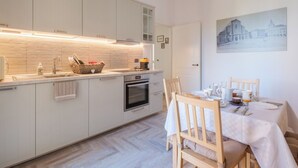 Una cocina moderna con una isla central, horno empotrado y un área de comedor con una mesa preparada para dos personas.