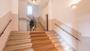 Una escalera con peldaños alfombrados y barandales de metal, que conduce a un rellano con una planta en maceta.